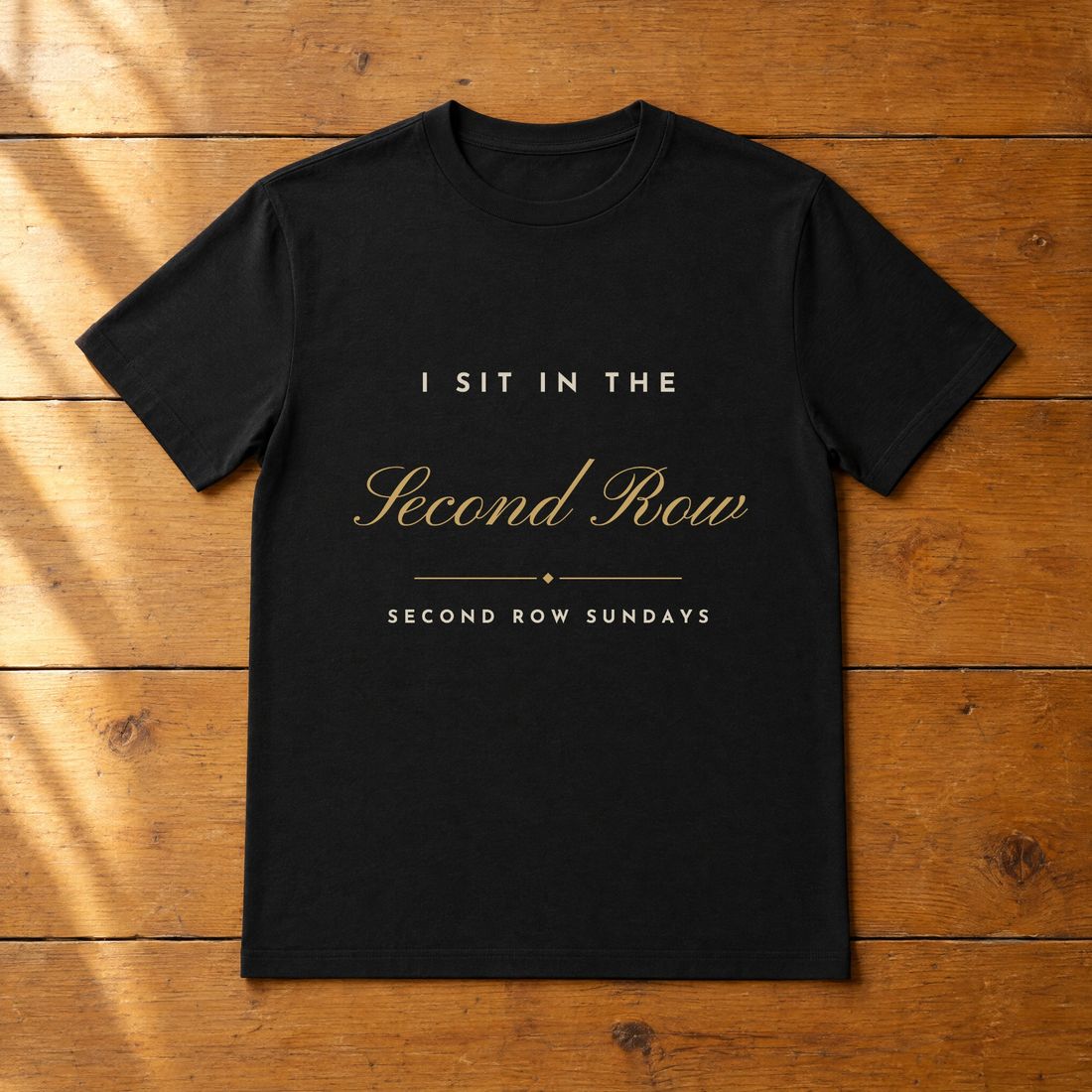 Black tee printed in cream and gold: I Sit in the Second Row.