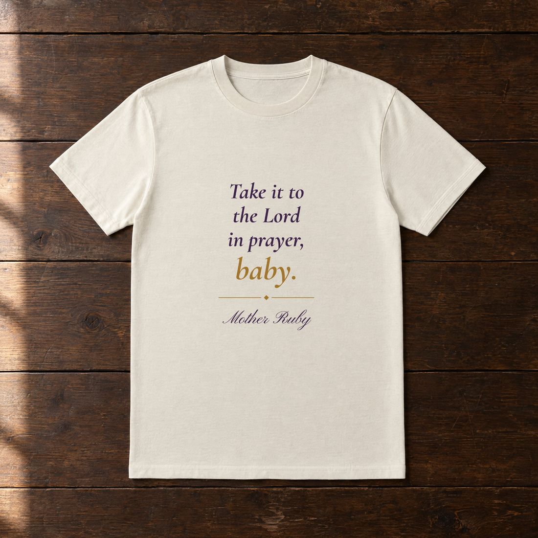 Cream tee printed in plum and gold: Take it to the Lord in prayer, baby. Signed Mother Ruby.