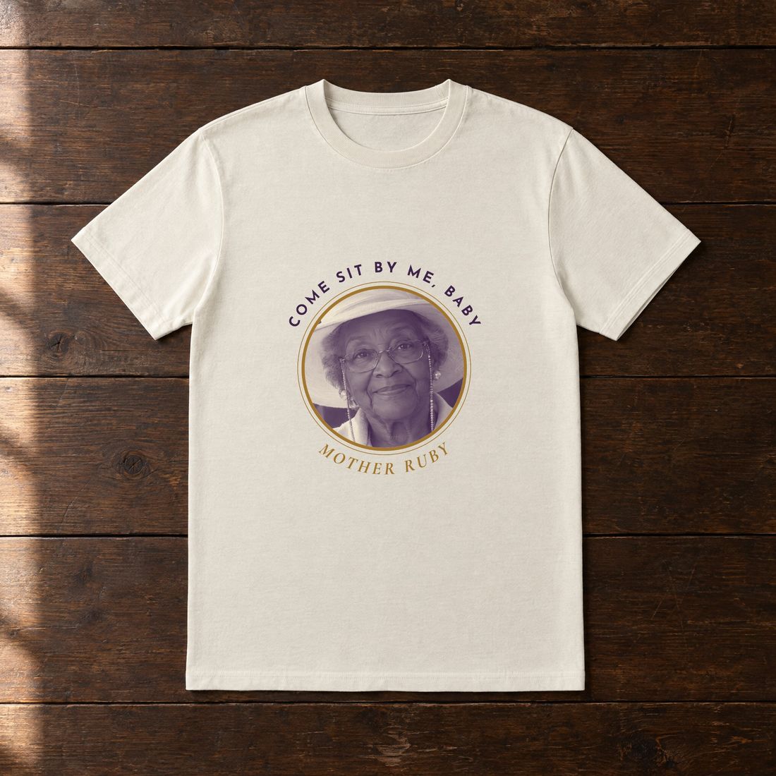 Cream tee with a round portrait of Mother Ruby and the words Come sit by me, baby.