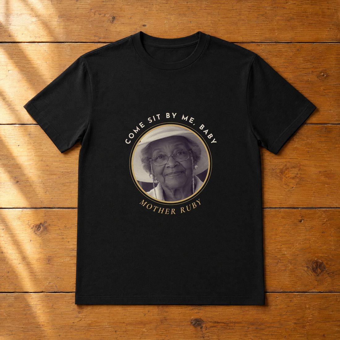 Black tee with a round portrait of Mother Ruby and the words Come sit by me, baby.